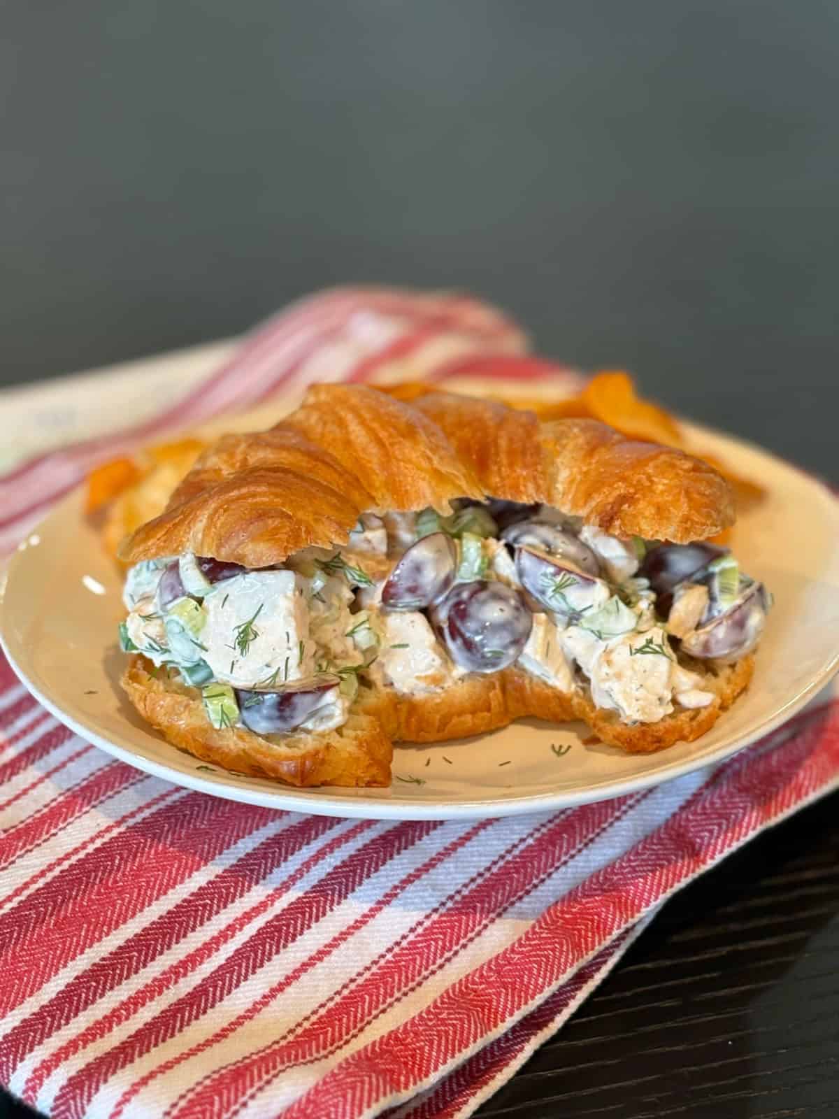 This creamy chicken salad from Pioneer Woman’s The Essential Recipes cookbook is filled with grapes, dill, and lemony dressing. A fresh, make-ahead lunch idea! chicken salad sandwich on a croissant on a plate