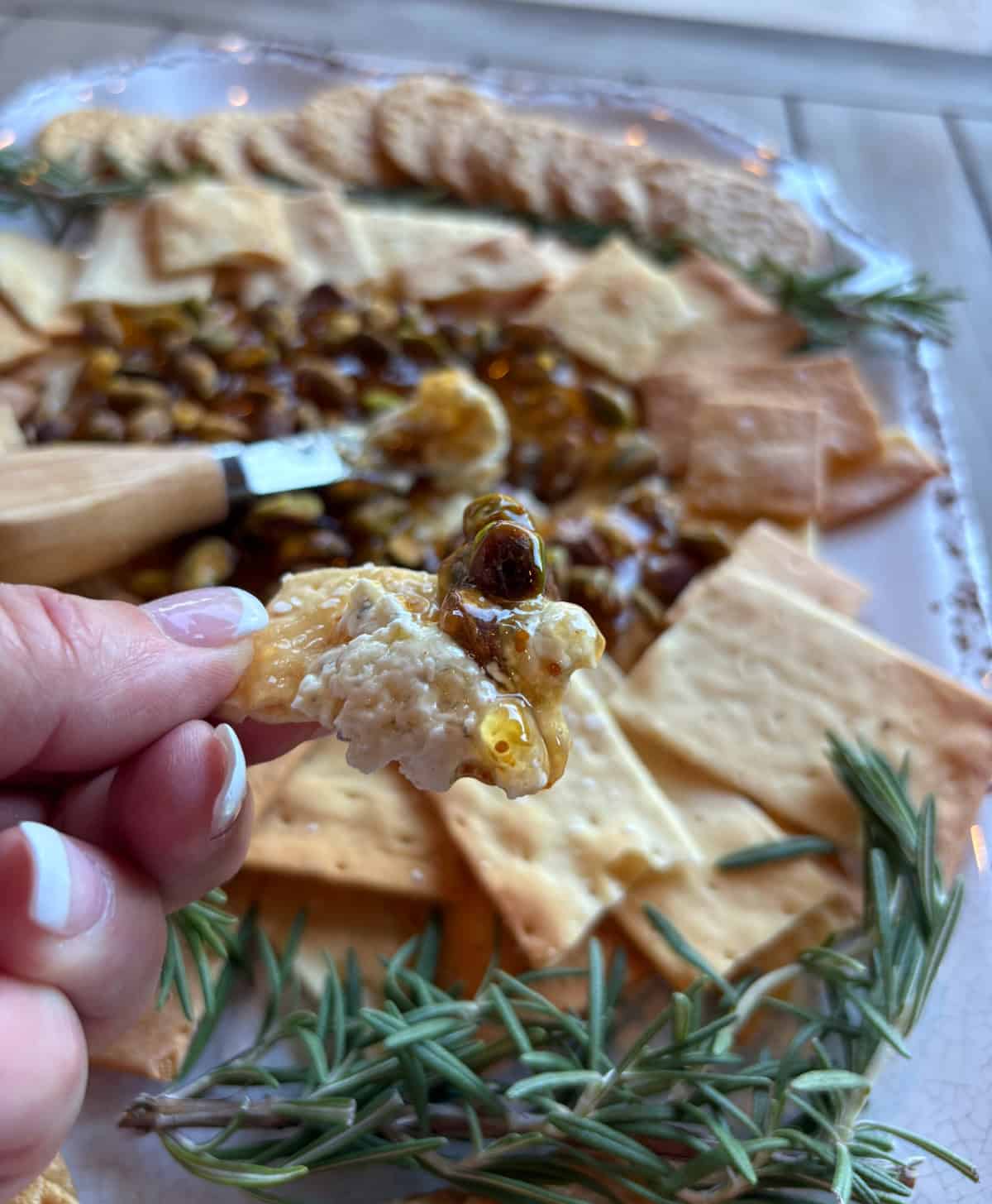 The easiest appetizer ever! Creamy Boursin topped with fig jam, pistachios, and hot honey. Sweet, salty, crunchy, and ready in minutes—perfect for parties! hand holding cracker with dip on it