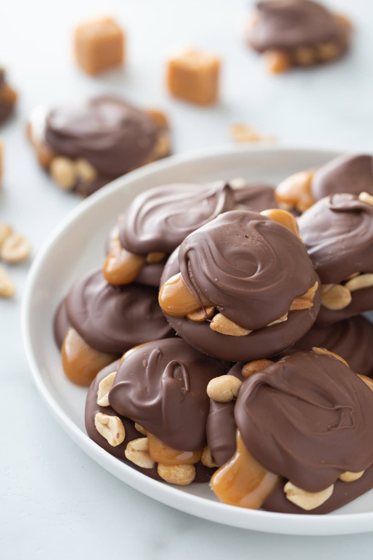 These Easy Caramel Peanut Clusters are layered with melted chocolate, roasted peanuts, and soft caramel—just like gourmet candy shop treats but so simple to make! chocolate caramel peanut clusters on a plate