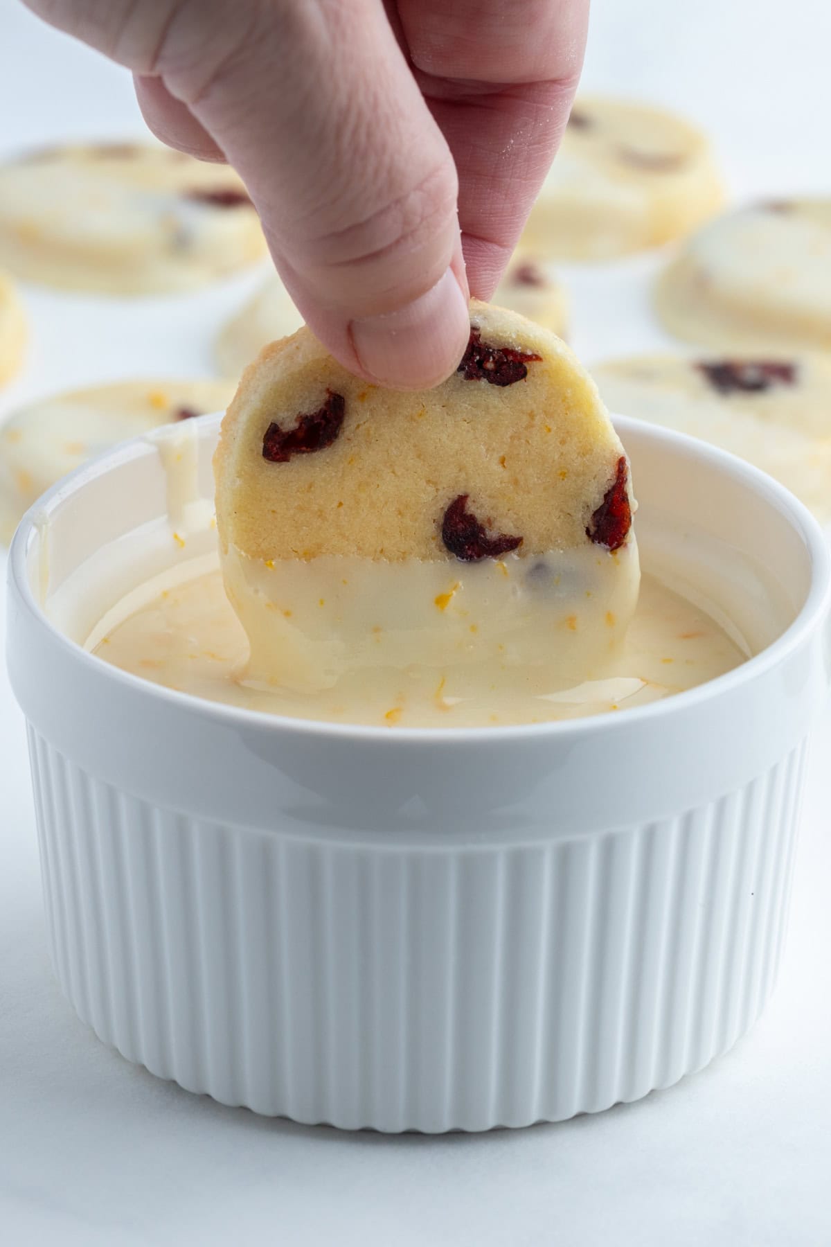 Bright, buttery Cranberry Orange Cookies loaded with dried cranberries and fresh orange zest, dipped in a sweet citrus glaze. A gorgeous slice-and-bake cookie for the holidays! dipping a cranberry orange cookie into glaze