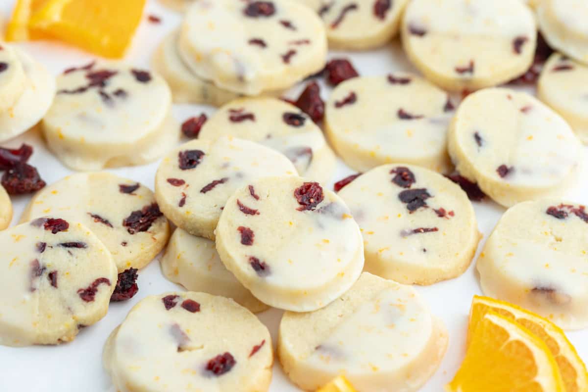 Bright, buttery Cranberry Orange Cookies loaded with dried cranberries and fresh orange zest, dipped in a sweet citrus glaze. A gorgeous slice-and-bake cookie for the holidays! several cranberry orange cookies