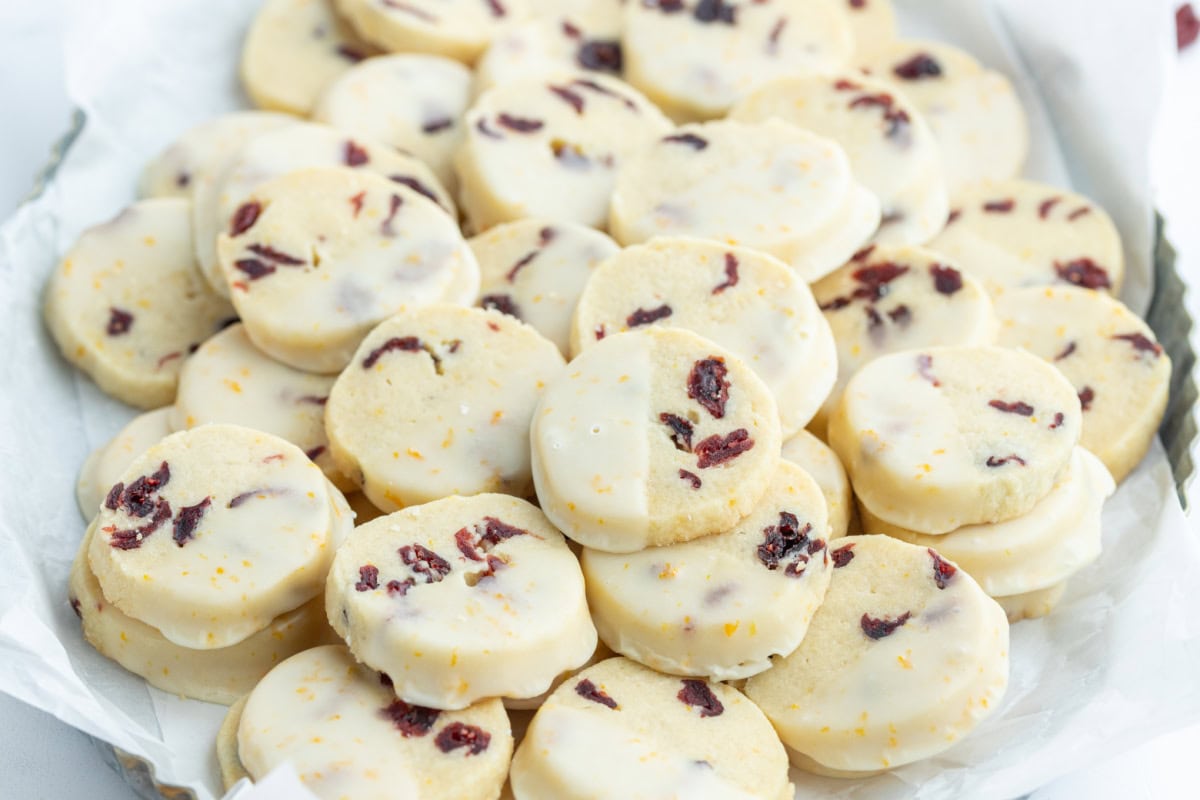 Bright, buttery Cranberry Orange Cookies loaded with dried cranberries and fresh orange zest, dipped in a sweet citrus glaze. A gorgeous slice-and-bake cookie for the holidays! cranberry orange cookies on a plate