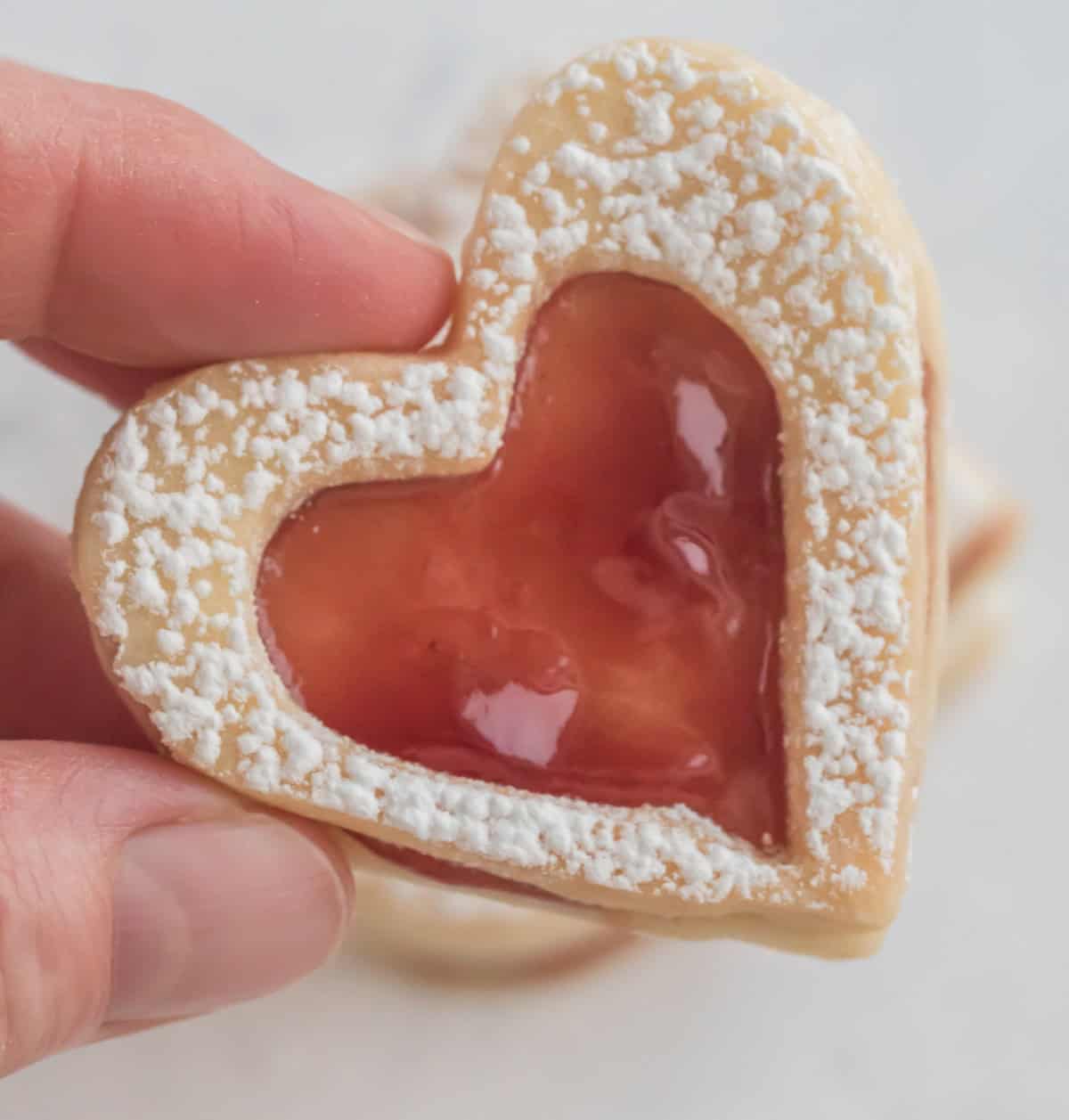 fingers holding linzer heart cookies