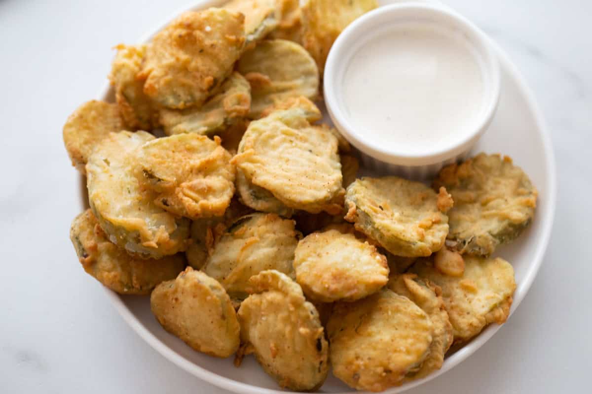 Deep Fried Pickles are crispy, golden and totally addictive. An easy appetizer recipe perfect for game day or snacking. deep fried pickles on a plate with a dish of dipping sauce