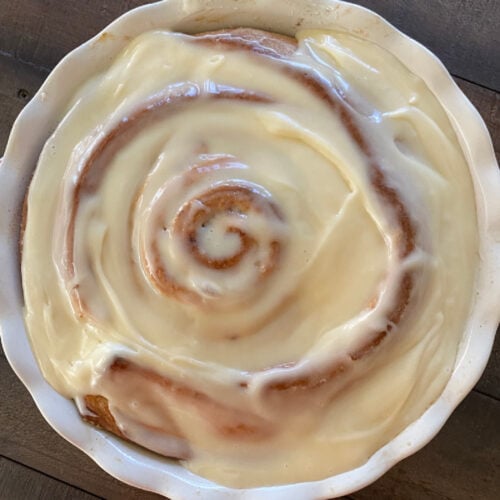 giant cinnamon roll in pie plate covered with cream cheese frosting