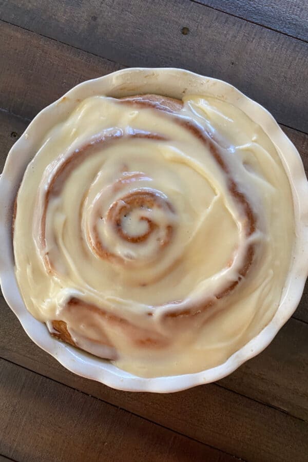 giant cinnamon roll in pie plate covered with cream cheese frosting