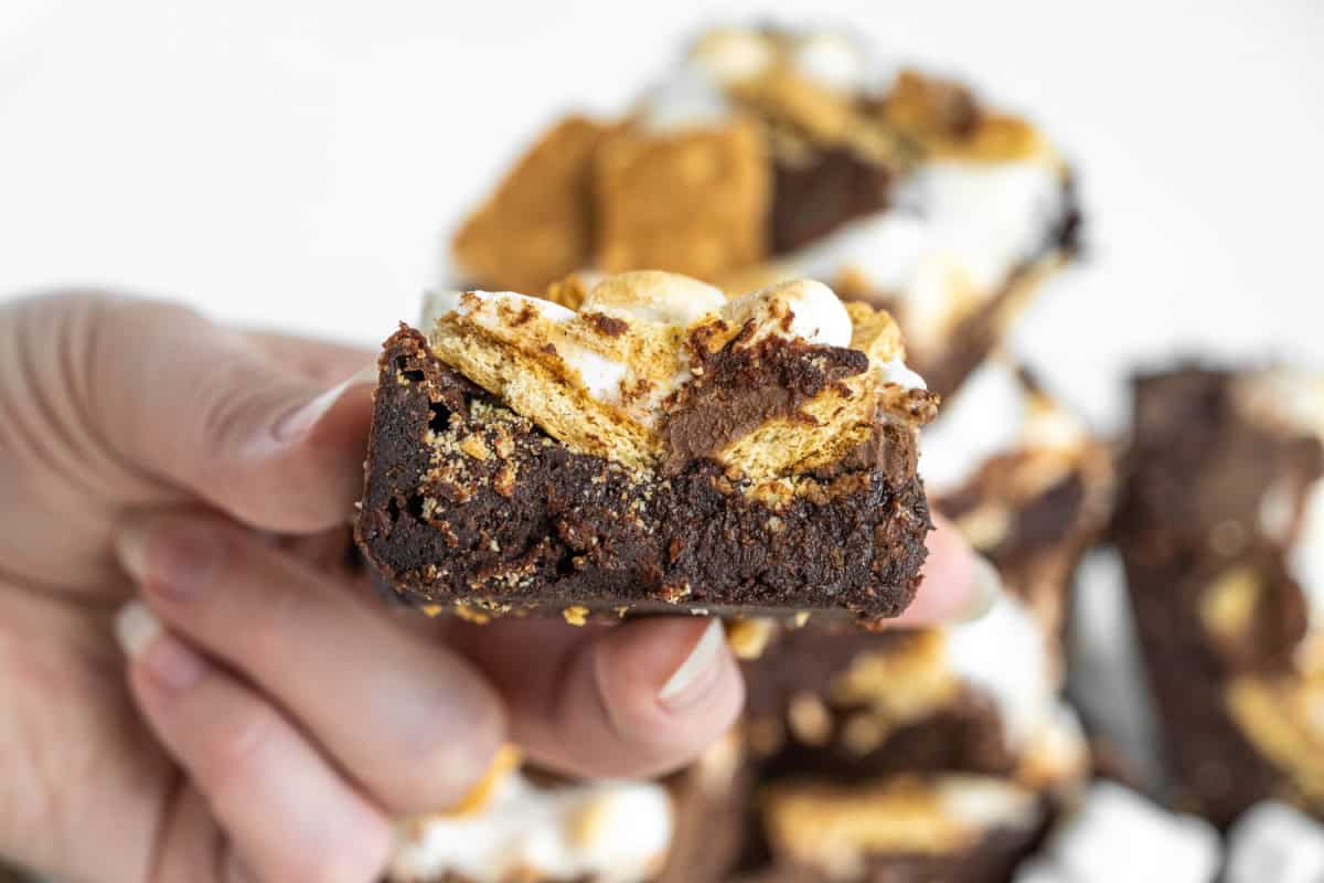 S’mores Brownies are gooey, fudgy and loaded with marshmallows, graham crackers and chocolate. An easy dessert that tastes like campfire s’mores. hand holding s'mores brownie