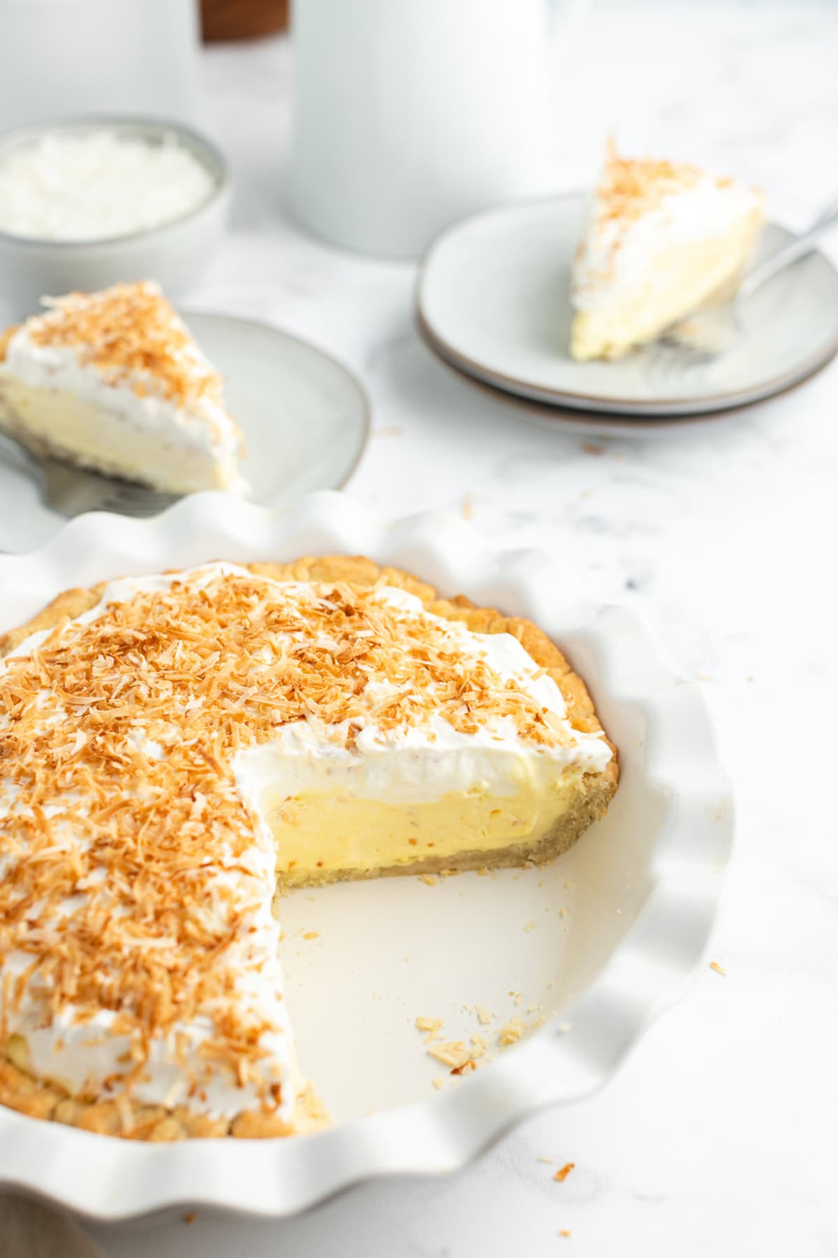 Coconut Cream Pie with a rich custard filling, whipped cream and toasted coconut. A classic homemade dessert that’s totally worth it. coconut cream pie with big slice taken out of it