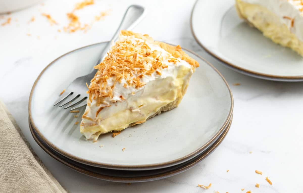 Coconut Cream Pie with a rich custard filling, whipped cream and toasted coconut. A classic homemade dessert that’s totally worth it. coconut cream pie slice on a plate