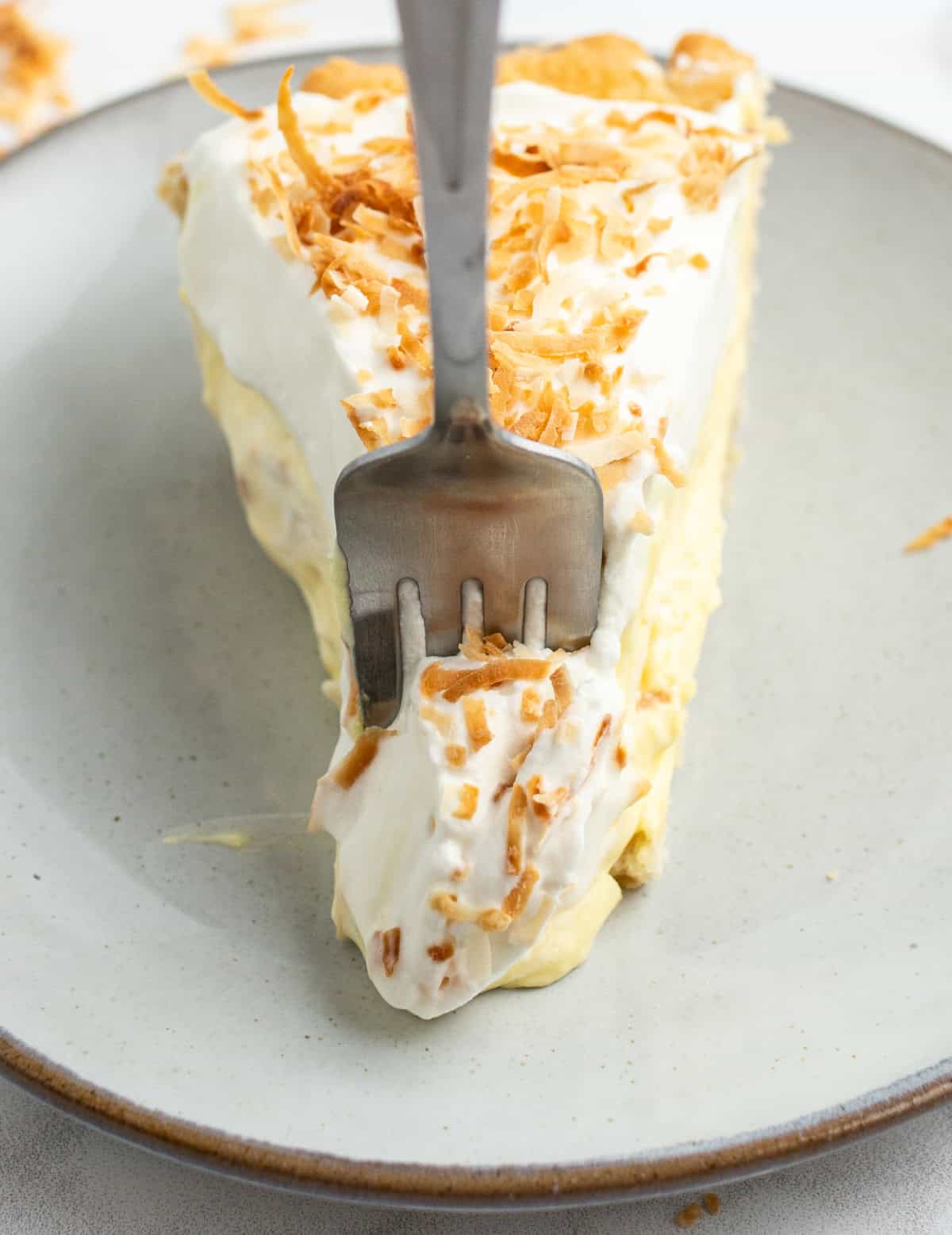 Coconut Cream Pie with a rich custard filling, whipped cream and toasted coconut. A classic homemade dessert that’s totally worth it. fork in a slice of coconut cream pie