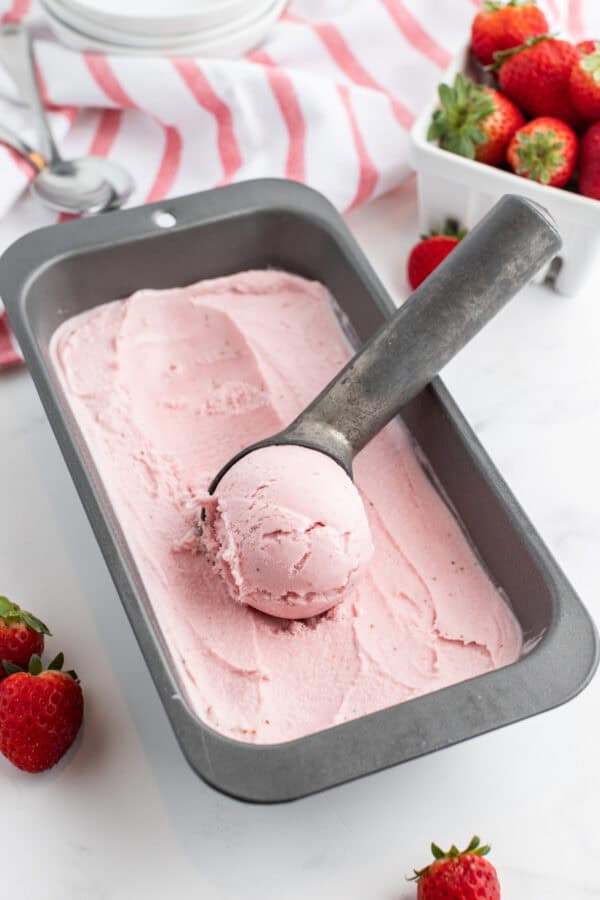 pan of homemade strawberry ice cream with ice cream scoop in it