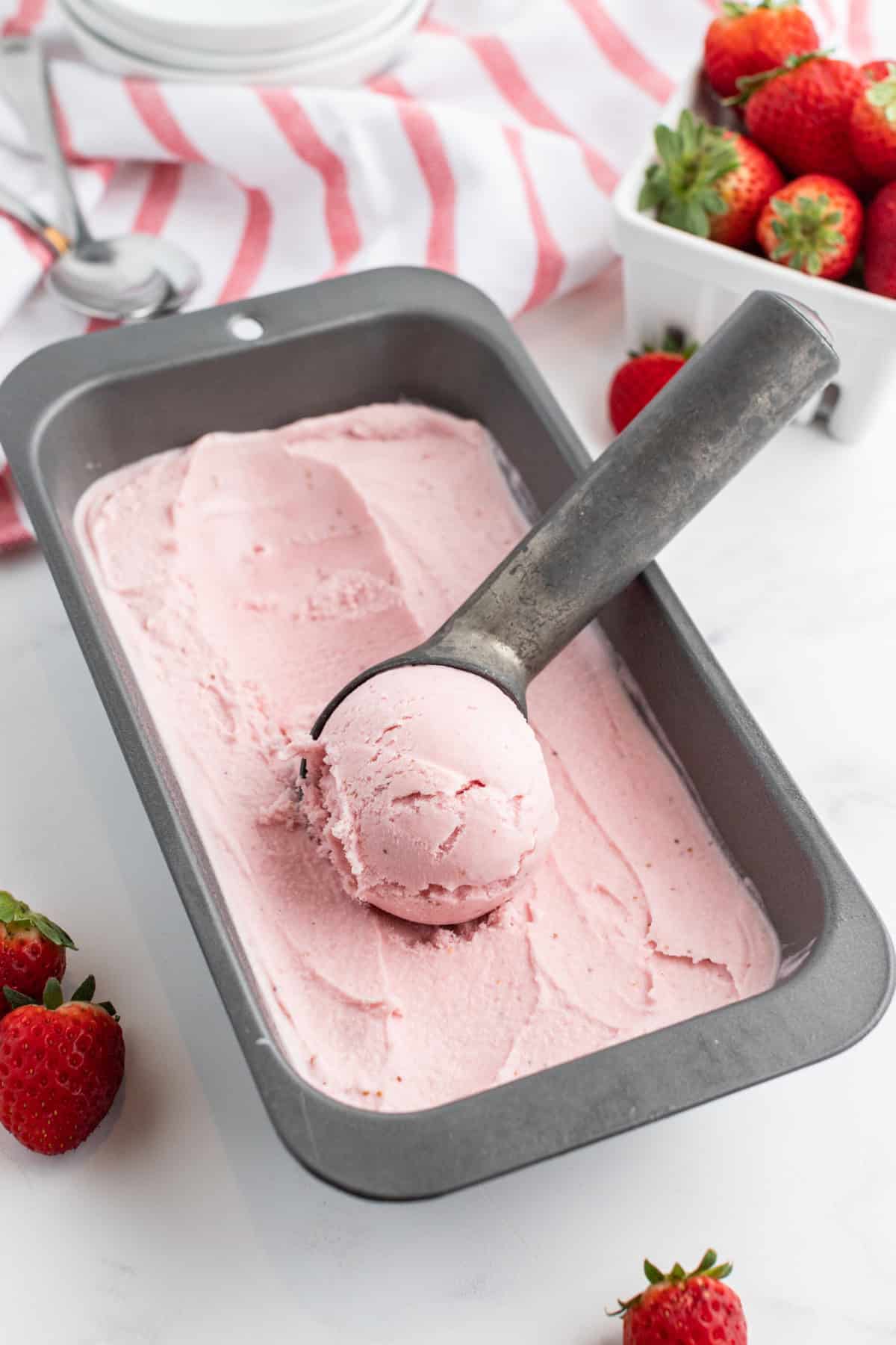 pan of homemade strawberry ice cream with ice cream scoop in it