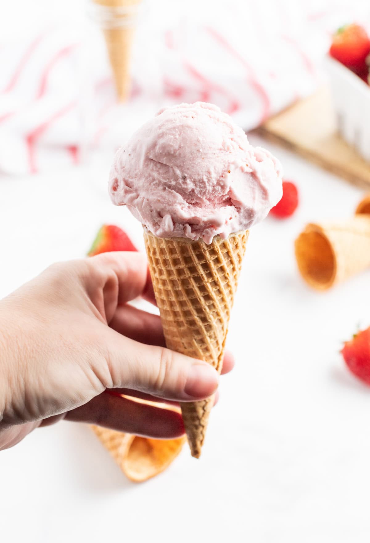 Homemade strawberry ice cream made with fresh strawberries and a creamy base. Smooth, easy and perfect for summer! hand holding a cone of homemade strawberry ice cream