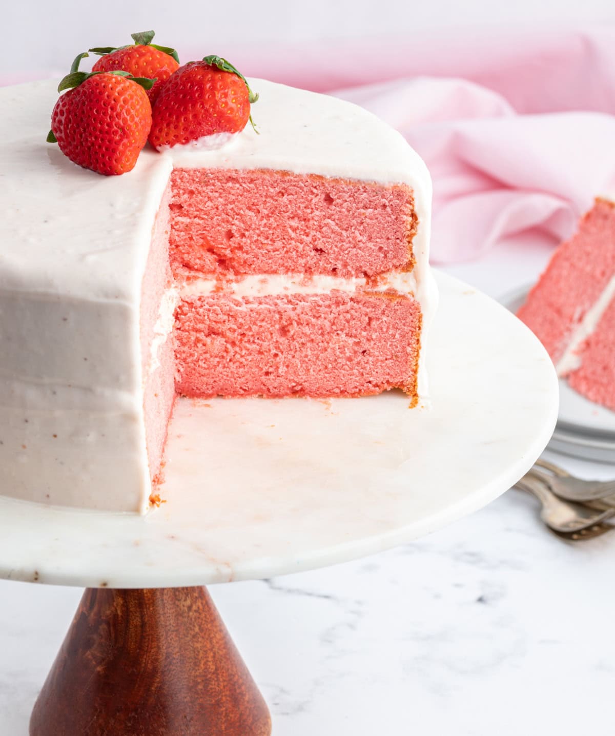 Strawberry Layer Cake is soft, moist and packed with strawberry flavor. A beautiful cake perfect for celebrations and special occasions. strawberry layer cake on a cake stand with one big slice taken out of it