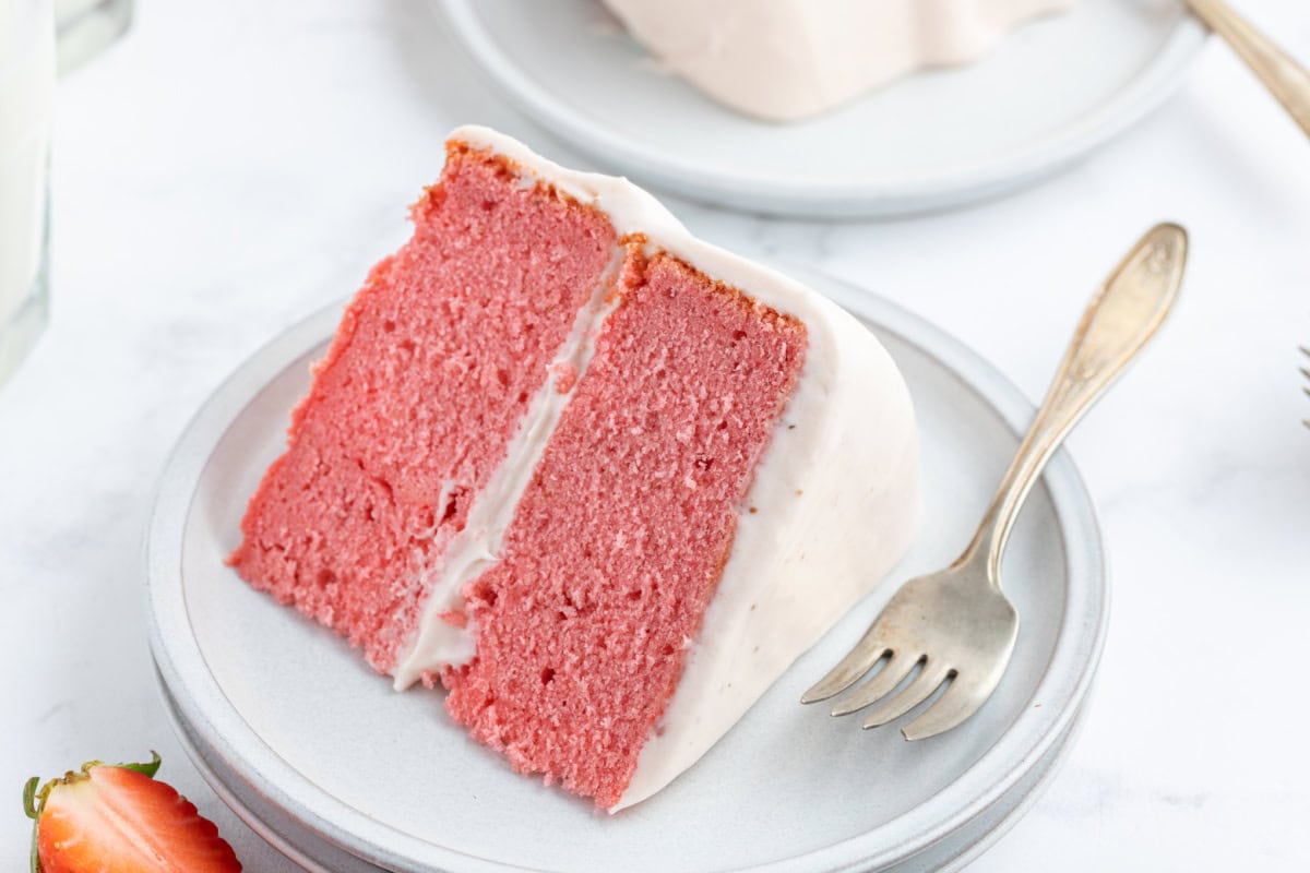 Strawberry Layer Cake is soft, moist and packed with strawberry flavor. A beautiful cake perfect for celebrations and special occasions. serving of strawberry layer cake on a plate with a fork