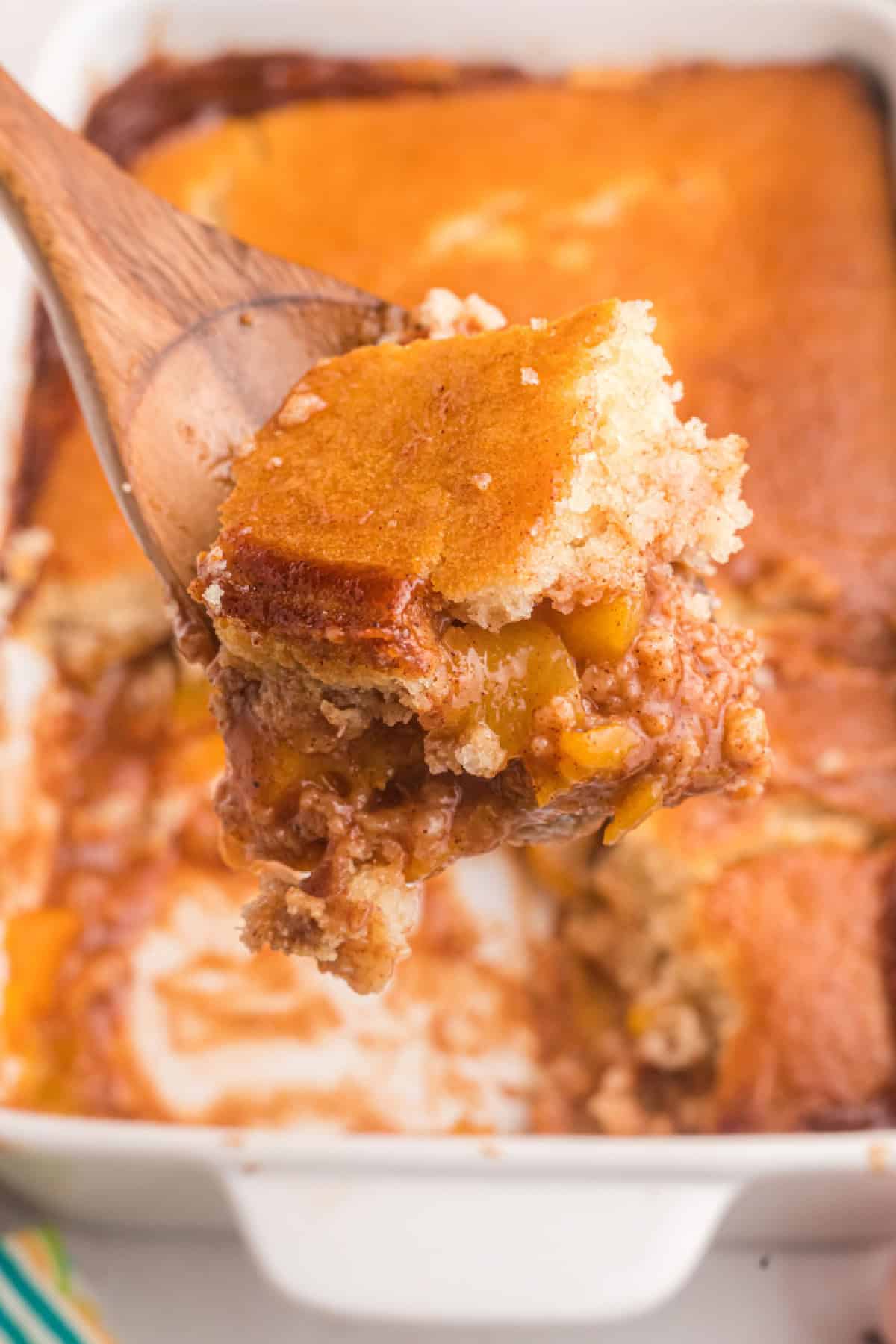 This Easy Peach Cobbler is packed with sweet peaches, warm cinnamon and nutmeg, and a buttery golden topping that tastes amazing with vanilla ice cream. Made with fresh or frozen peaches, it's the perfect summer dessert recipe for family gatherings, potlucks and holidays. Save this homemade peach cobbler recipe for later! #peachcobbler #peachdessert #summerdesserts #bakingrecipes #comfortfood spooning peach cobbler out of pan
