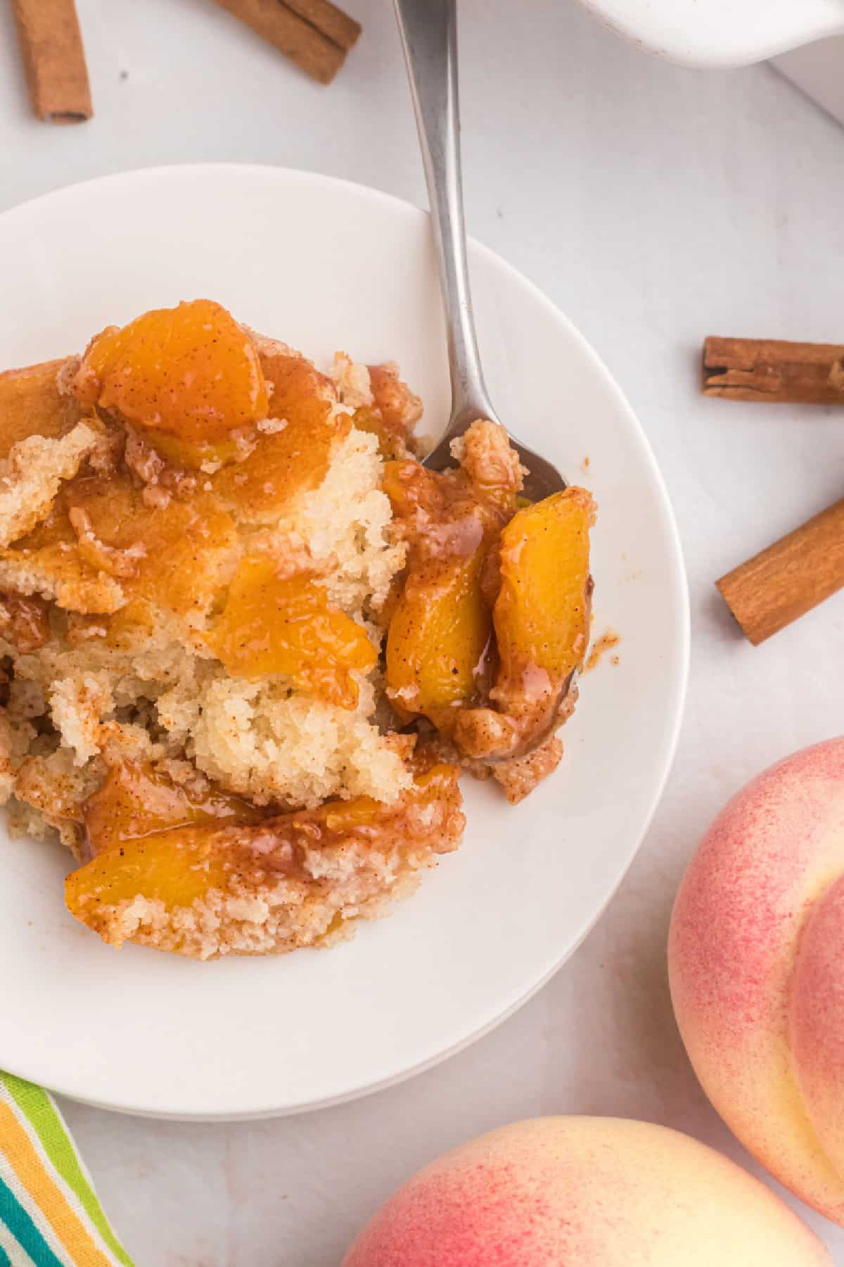 This Easy Peach Cobbler is packed with sweet peaches, warm cinnamon and nutmeg, and a buttery golden topping that tastes amazing with vanilla ice cream. Made with fresh or frozen peaches, it's the perfect summer dessert recipe for family gatherings, potlucks and holidays. Save this homemade peach cobbler recipe for later! #peachcobbler #peachdessert #summerdesserts #bakingrecipes #comfortfood serving of peach cobbler on plate