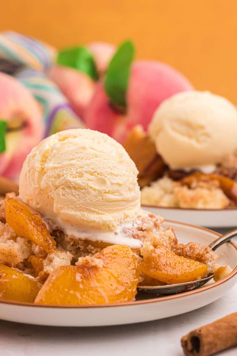 This Easy Peach Cobbler is packed with sweet peaches, warm cinnamon and nutmeg, and a buttery golden topping that tastes amazing with vanilla ice cream. Made with fresh or frozen peaches, it's the perfect summer dessert recipe for family gatherings, potlucks and holidays. Save this homemade peach cobbler recipe for later! #peachcobbler #peachdessert #summerdesserts #bakingrecipes #comfortfood easy peach cobbler on plate with ice cream